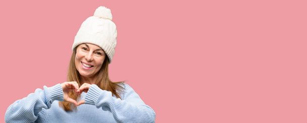 Femme d'âge moyen portant bonnet d'hiver en laine heureux montrant l'amour avec les mains en forme de coeur exprimant symbole sain et de mariage
 - Photo, image