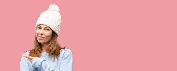 Donna di mezza età indossando berretto invernale in lana che punta via lato con il dito
 - Foto, immagini