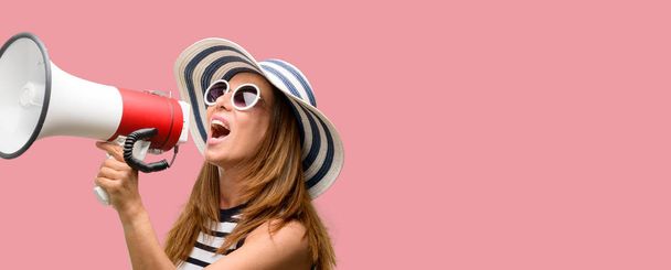 Крутая женщина средних лет в летней шляпе и солнцезащитных очках громко кричит, держа мегафон, выражая успех и позитивную концепцию, идею для маркетинга или продаж
 - Фото, изображение