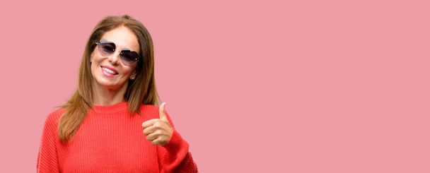 Femme d'âge moyen portant des lunettes de soleil de coeur souriant montrant largement pouces vers le haut geste à la caméra, expression de similaires et approbation
 - Photo, image