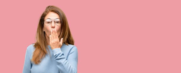 Женщина средних лет в шерстяном свитере и крутых очках покрывает рот в шоке, выглядит застенчивым, выражает тишину и ошибочные концепции, напуганный
 - Фото, изображение