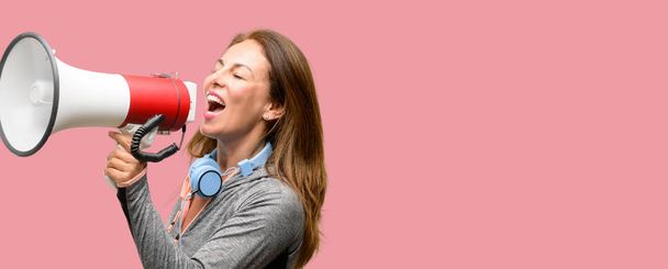 Middle age gym fit woman with workout headphones communicates shouting loud holding a megaphone, expressing success and positive concept, idea for marketing or sales - Photo, Image