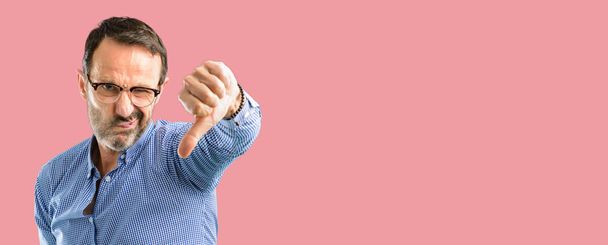 Jóvágású középkorú férfi hüvelykujját lefelé boldogtalan jele ellenszenv, a negatív kifejezés és a helytelenítés mutatja - Fotó, kép