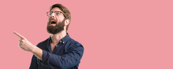 Young hipster man with big beard pointing away side with finger - Photo, Image