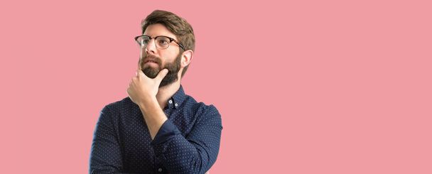 Young hipster man with big beard thinking and looking up expressing doubt and wonder - Photo, Image