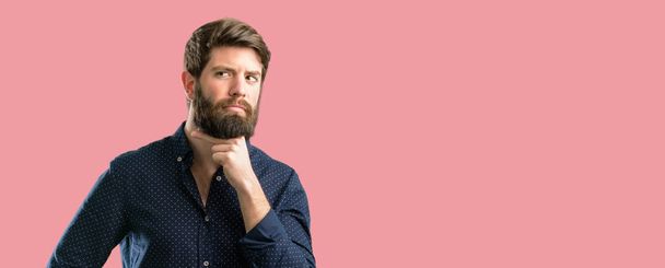 Homem jovem hipster com barba grande pensando pensativo com cara inteligente, expressando pergunta e dúvida. Imagine a solução
 - Foto, Imagem