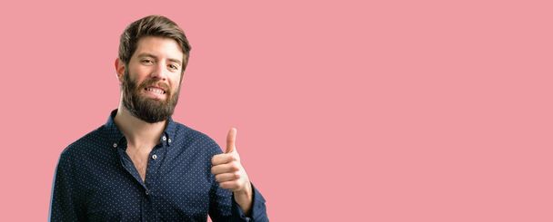 Young hipster man with big beard smiling broadly showing thumbs up gesture to camera, expression of like and approval - Foto, imagen