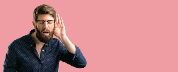 Mladí bokovky muž s velkými vousy drží ruku do blízkosti ucha snaží naslouchat zajímavé novinky vyjádření komunikační koncept a drby - Fotografie, Obrázek