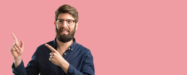 Homem jovem hipster com barba grande apontando para o lado com o dedo
 - Foto, Imagem