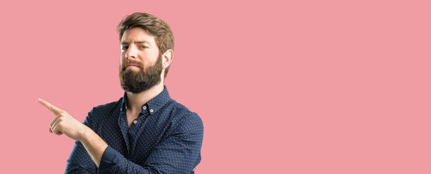 Young hipster man with big beard pointing away side with finger - Photo, Image