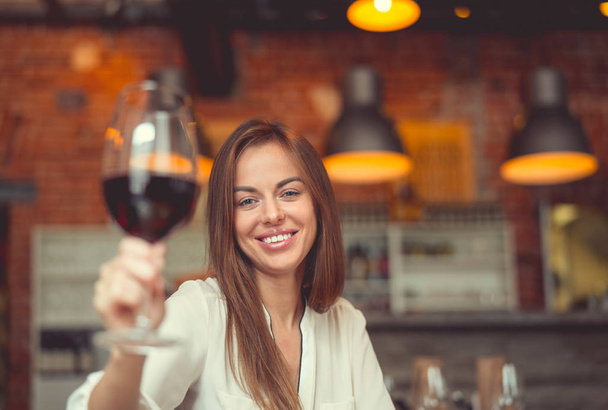 Νεαρό χαμογελαστό κορίτσι με ένα ποτήρι κρασί σε ένα εστιατόριο - Φωτογραφία, εικόνα