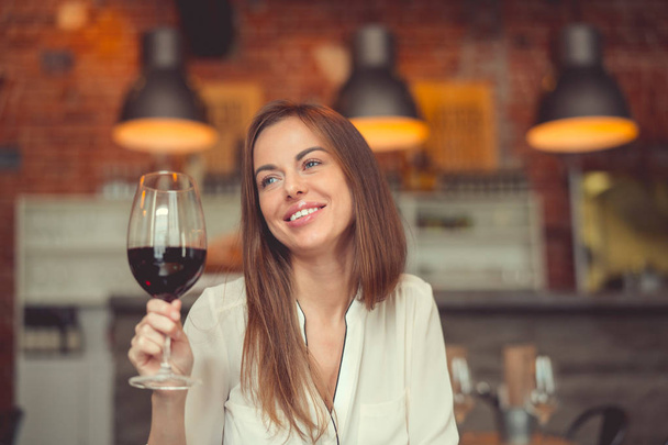 Χαμογελαστό κορίτσι με ένα ποτήρι κόκκινο κρασί σε ένα εστιατόριο - Φωτογραφία, εικόνα