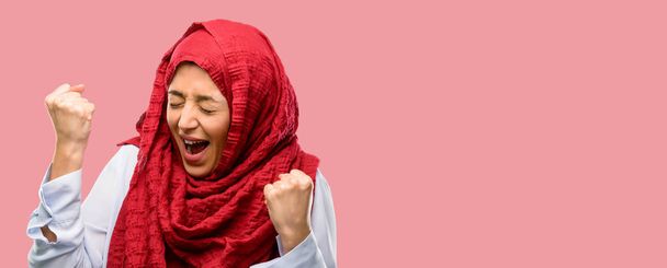 Mujer árabe joven usando hijab feliz y emocionado expresando gesto ganador. Exitoso y celebrando la victoria, triunfante
 - Foto, imagen