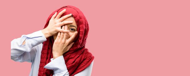 Nuori arabi nainen yllään hijab hymyilevä ottaa ujo ilme kurkistaa sormiensa läpi, peittää kasvot kädet etsivät hämmentävän laajasti
 - Valokuva, kuva