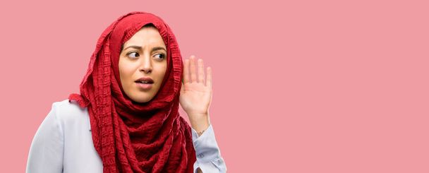Mujer árabe joven con hijab agarrado de la mano cerca de la oreja tratando de escuchar noticias interesantes que expresan el concepto de comunicación y chismes
 - Foto, imagen
