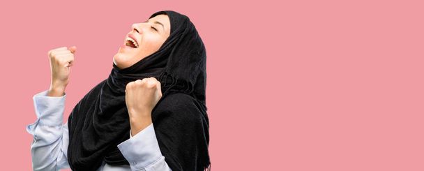 若いアラブ女性の幸せと勝利のジェスチャーを表現する興奮のヒジャーブを身に着けています。成功、勝利、勝利を祝って - 写真・画像