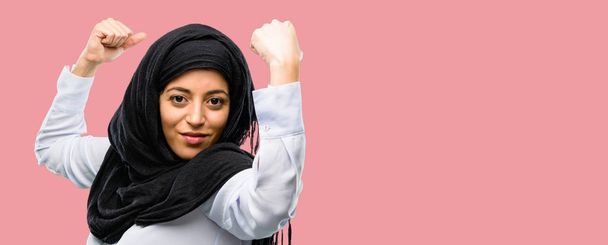 Jonge Arabische vrouw het dragen van hijab tonen biceps uiting van kracht en sportschool concept, gezond leven zijn goed - Foto, afbeelding