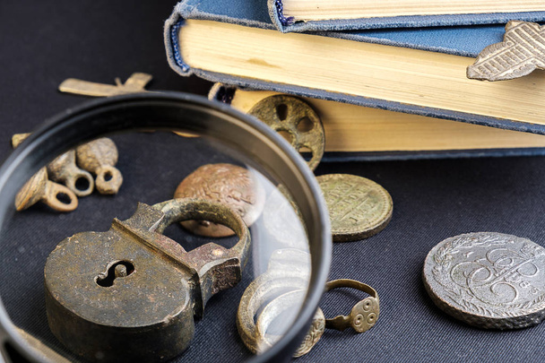 under a magnifying glass is considered an old copper padlock around an old coin and a book - Foto, Imagen
