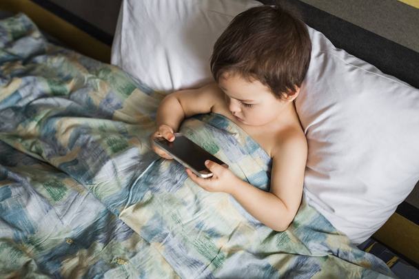 modern boy playing phone lying on the bed in morning - Фото, зображення
