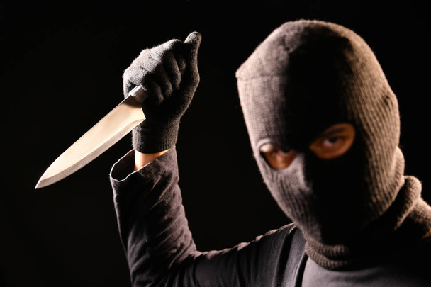 O ladrão segurar a faca na mão sobre fundo preto
 - Foto, Imagem
