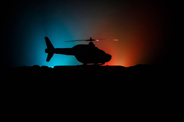 Askeri helikopterin silueti çatışma bölgesinden uçmaya hazır. Çölden başlayan sisli arka ışıklandırmalı helikopterle dekore edilmiş gece görüntüleri. Seçici odaklanma. Savaş konsepti - Fotoğraf, Görsel