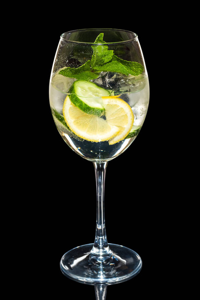 Cold Lemon and cucumber cocktail with a sparkling wine with ice cubes in wine glass isolated on black - 写真・画像