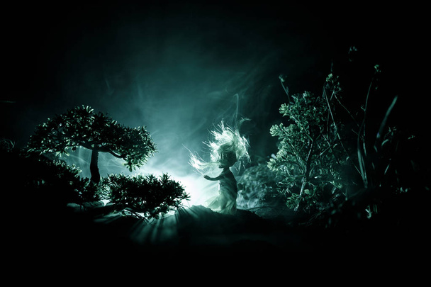 Horreur Halloween décoré image conceptuelle. Seule fille avec la lumière dans la forêt la nuit. Silhouette de fille debout entre les arbres avec une lumière surréaliste sur le fond. Concentration sélective
. - Photo, image