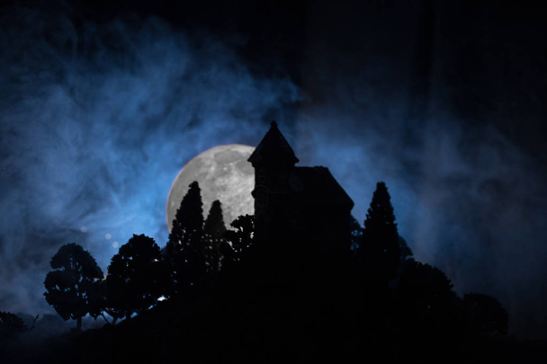Antigua casa con un Fantasma en el bosque por la noche o Casa de terror embrujada abandonada en la niebla. Antiguo edificio místico en el bosque de árboles muertos. Concepto de Halloween de horror. Enfoque selectivo
 - Foto, imagen