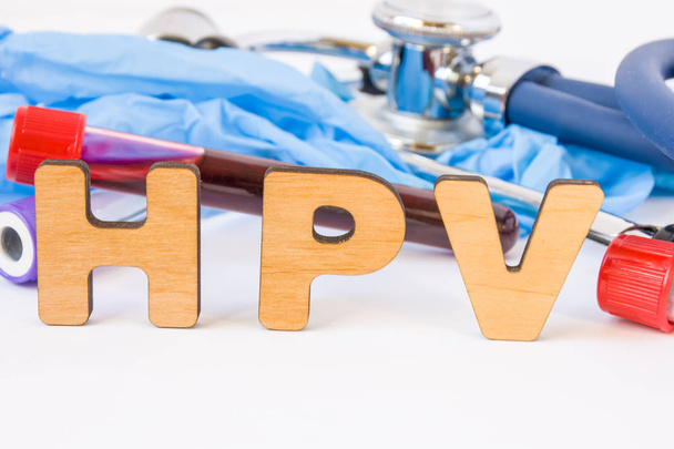 Abbreviation or acronym of HPV, in laboratory, scientific, research or medical practice means human papilloma virus, is in foreground with laboratory test tubes, medical stethoscope and gloves - Photo, Image
