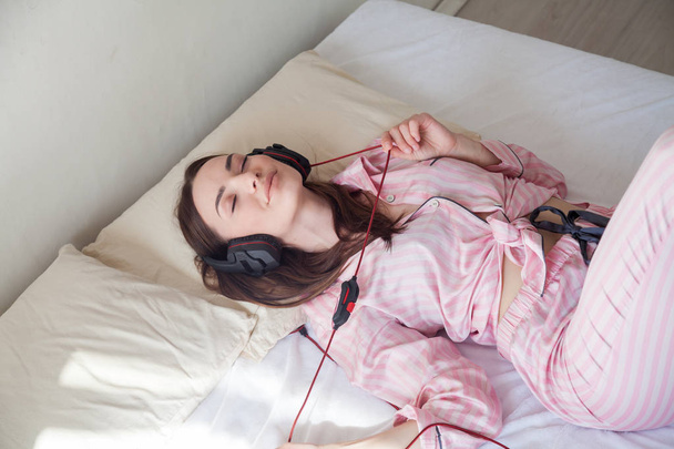 mulher morena em rosa Pajamas ouvindo música com fones de ouvido
 - Foto, Imagem