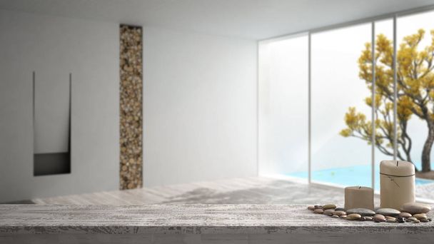 Wooden vintage table top or shelf with candles and pebbles, zen mood, over blurred empty room with fireplace and big panoramic window on garden and swimming pool, white architecture interior design - Photo, Image