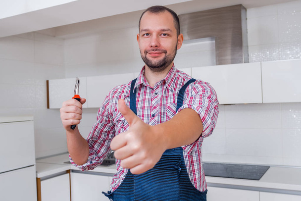 schöner Arbeiter in Uniform, der in der Küche eine Zange hält - Foto, Bild