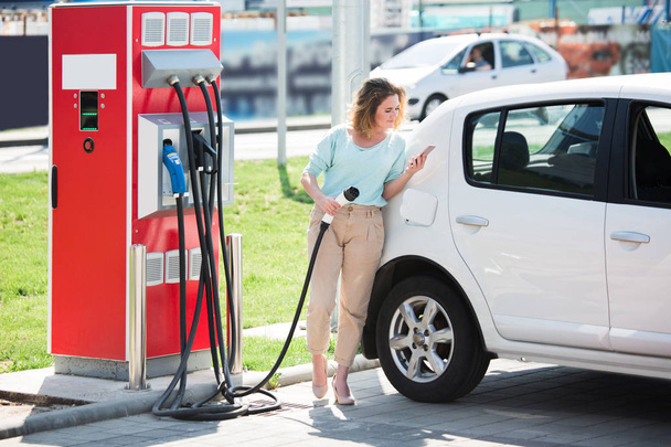 A woman at the charging station for electric vehicles - Foto, imagen