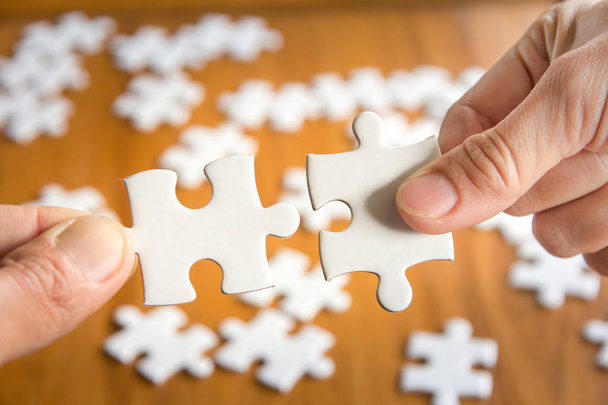 Close up of hand connecting jigsaw puzzle with wooden background - Photo, Image