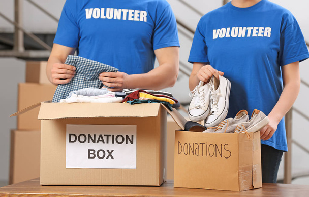 Volunteers putting clothes and shoes in donation boxes indoors - Foto, afbeelding