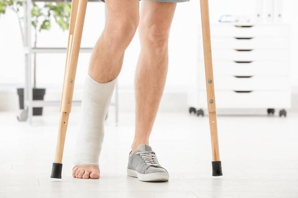 Man with broken leg in cast standing on crutches, indoors - Foto, imagen