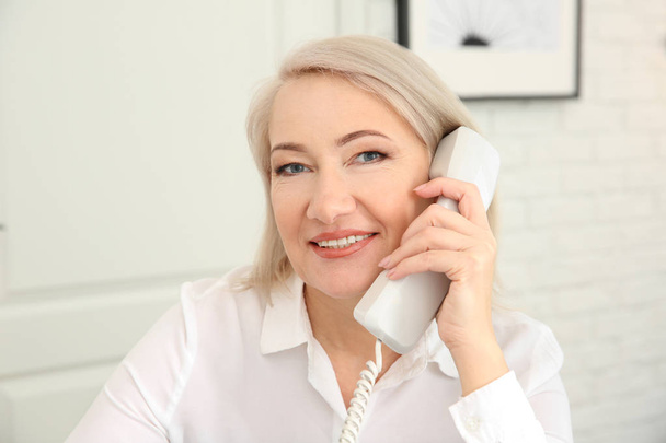 Mature woman talking on phone at workplace - Фото, изображение