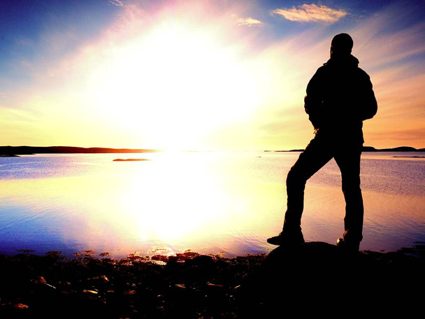 Silhouette dell'uomo in abiti da esterno su scogliera rocciosa sopra il mare. Escursionismo pensando durante il tramonto sullo sfondo. Viaggiare via concetto
. - Foto, immagini