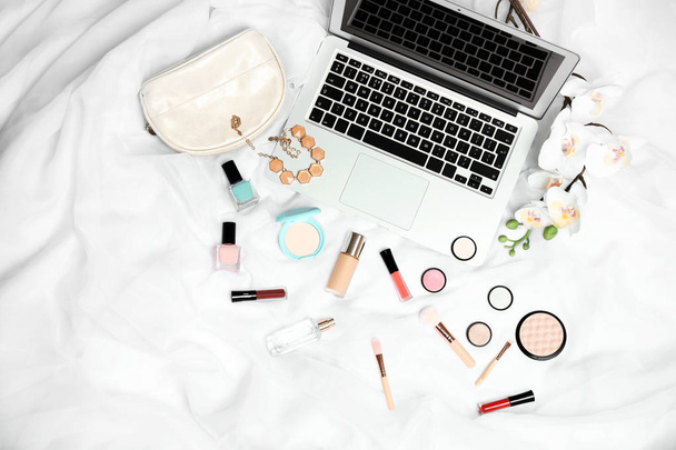 Flat lay composition with laptop and makeup products for woman on bed - Photo, Image
