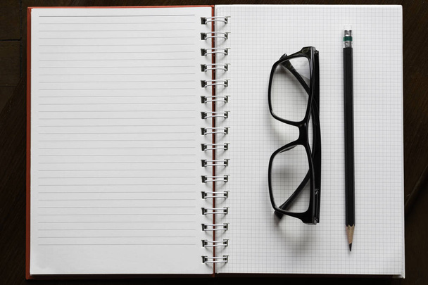 pencil and glasses on open book with line on brown wood - Фото, зображення