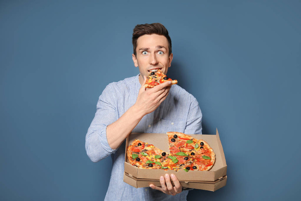 Attractive young man with delicious pizza on color background - Foto, afbeelding