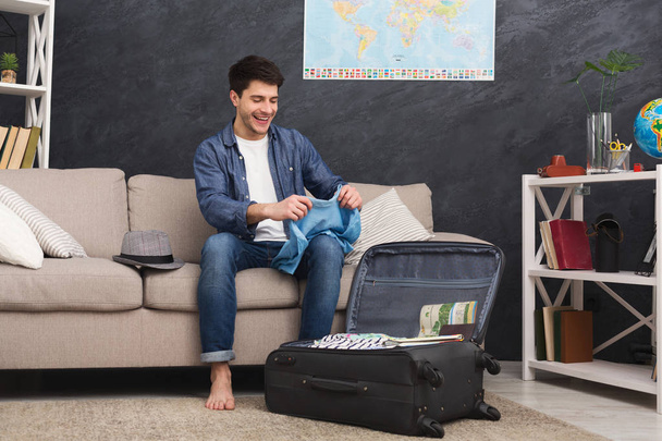 Happy man packing clothes into travel bag - Photo, Image