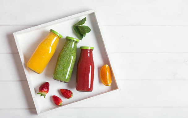 Fresh orange, strawberry and broccoli smoothie in bottles with fruits and mint in a white wooden rustic box and on a white background, copy space for text. - 写真・画像