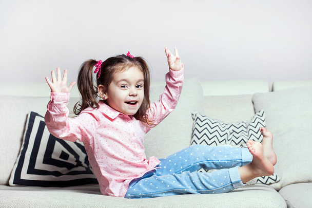 Pretty happy little girl in casual wearing sitting on sofa with toy dog and smiling. - Fotoğraf, Görsel