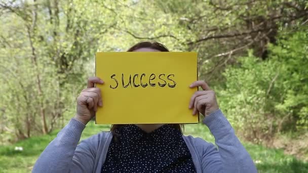 Fiatal nő, egy sárga papírlapot gazdaság sikerrel rajta kézzel írott - Felvétel, videó