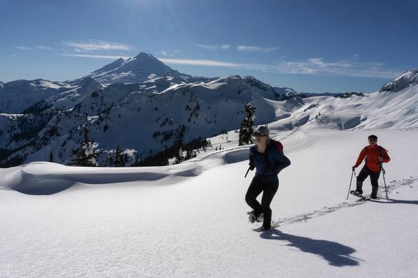 Adventurous man and woman are snowshoeing in the snow. Taken in Artist Point, Northeast of Seattle, Washington, United States of America. - Фото, зображення