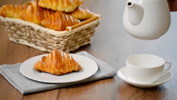 Croissant met thee. Ontbijt concept. Gieten van thee in kopje thee - Video