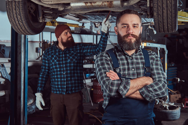 Two bearded brutal mechanics repair a car on a lift in the garage. Repairing car suspension. - Photo, Image