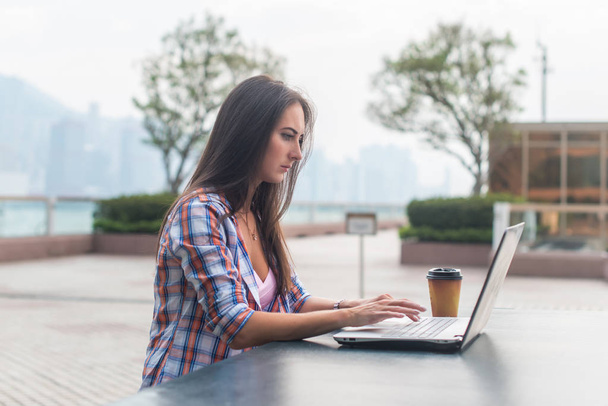 Mujer joven usando un ordenador portátil que trabaja al aire libre. Mujer mirando a la pantalla y escribiendo en el teclado
 - Foto, imagen