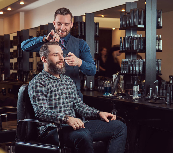 Barbeiro profissional trabalhando com um cliente em um salão de cabeleireiro. Cabelo de estilo com um aparador e um pente
. - Foto, Imagem